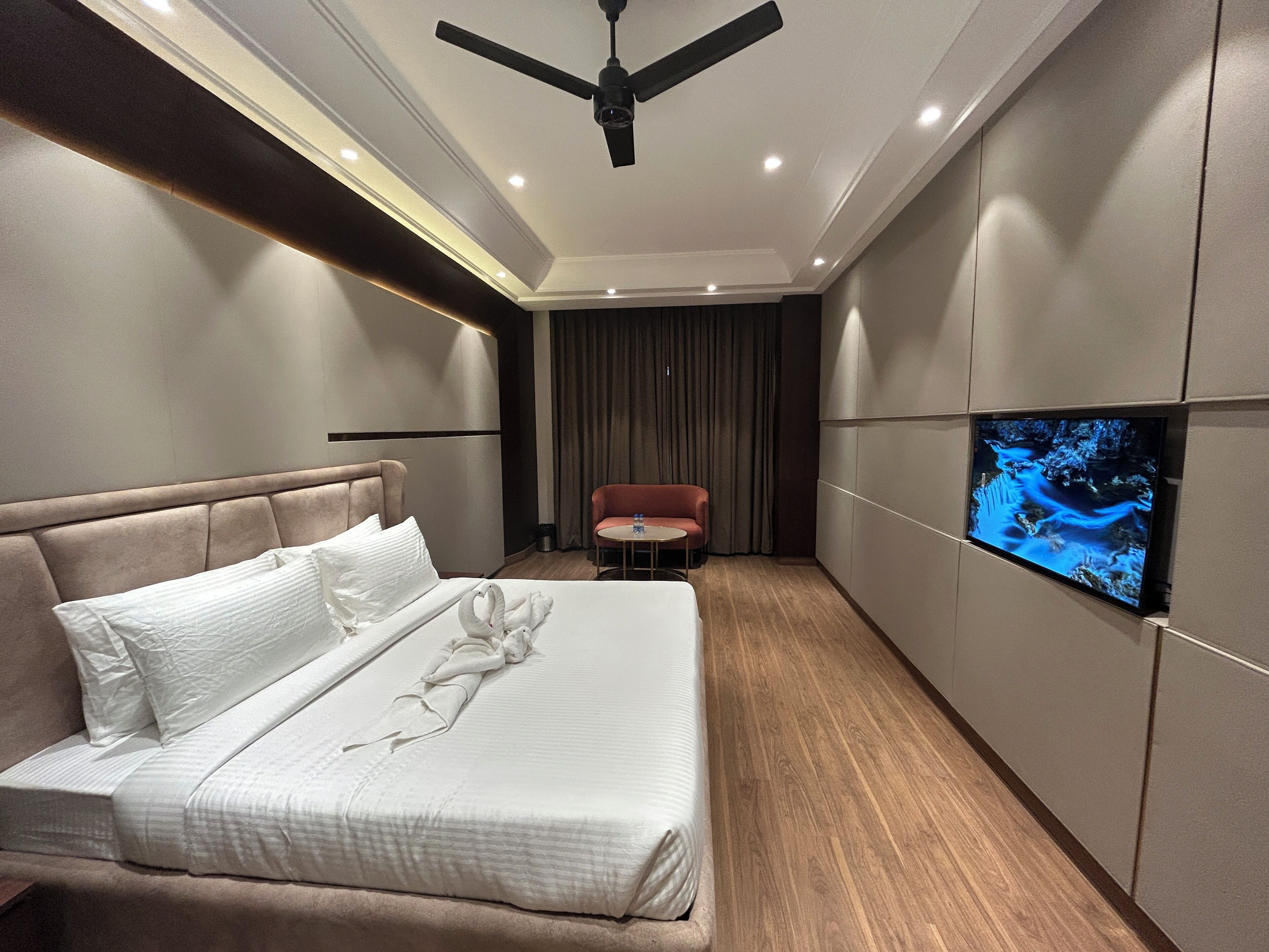 A hotel room with a bed, a ceiling fan, a television, and a small table.