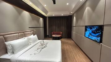 A hotel room with a bed, a ceiling fan, a television, and a small table.