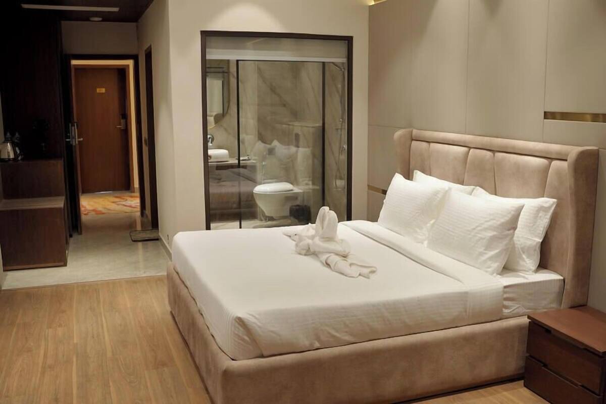 Una habitación de hotel moderna con una cama grande, cabina de ducha de cristal y suelo de madera.
