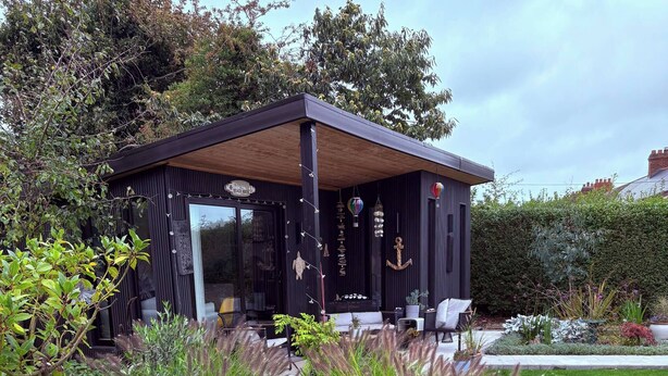 Een modern huis met een overdekte patio, omgeven door een verzorgde tuin met diverse planten en bloemen.