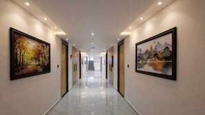 A hotel corridor with framed artwork on the walls, a polished floor, and a staircase at the end. - White Panda Hotels Shree Radhe (Dwarka)