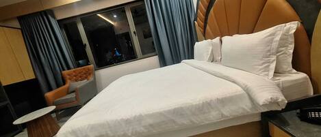 Un hotel moderno con una cama grande, una mesita, una silla y vistas de la ciudad a través de la ventana.