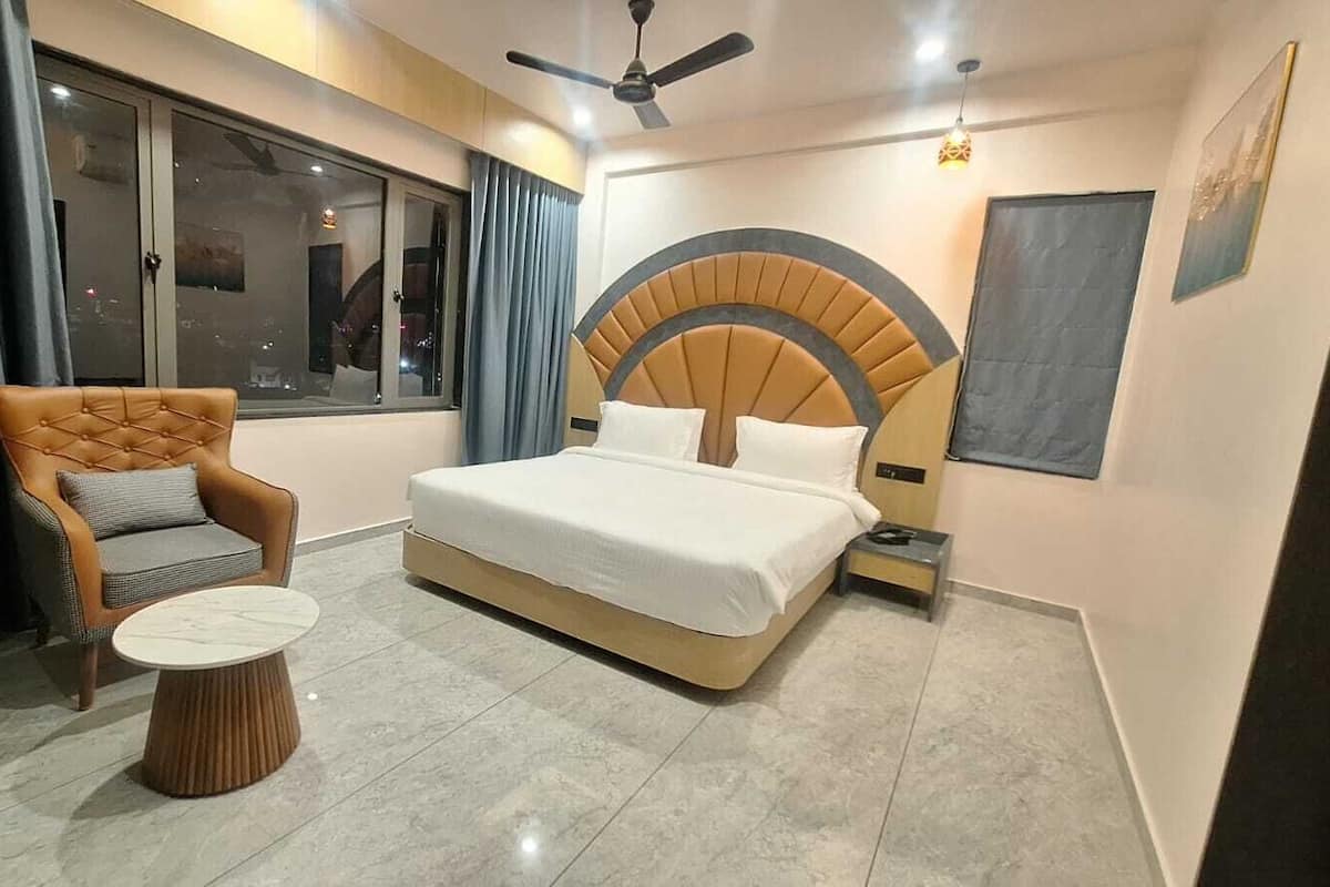 A modern bedroom with a large bed, a tufted armchair, a round side table, and a large window with curtains.