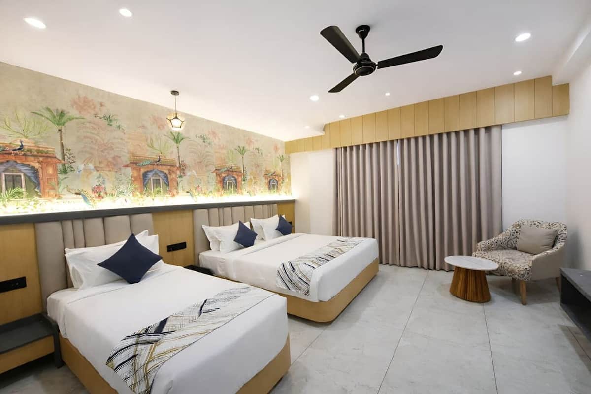 A hotel room with two beds, a ceiling fan, a mural, a chair, and a small table.