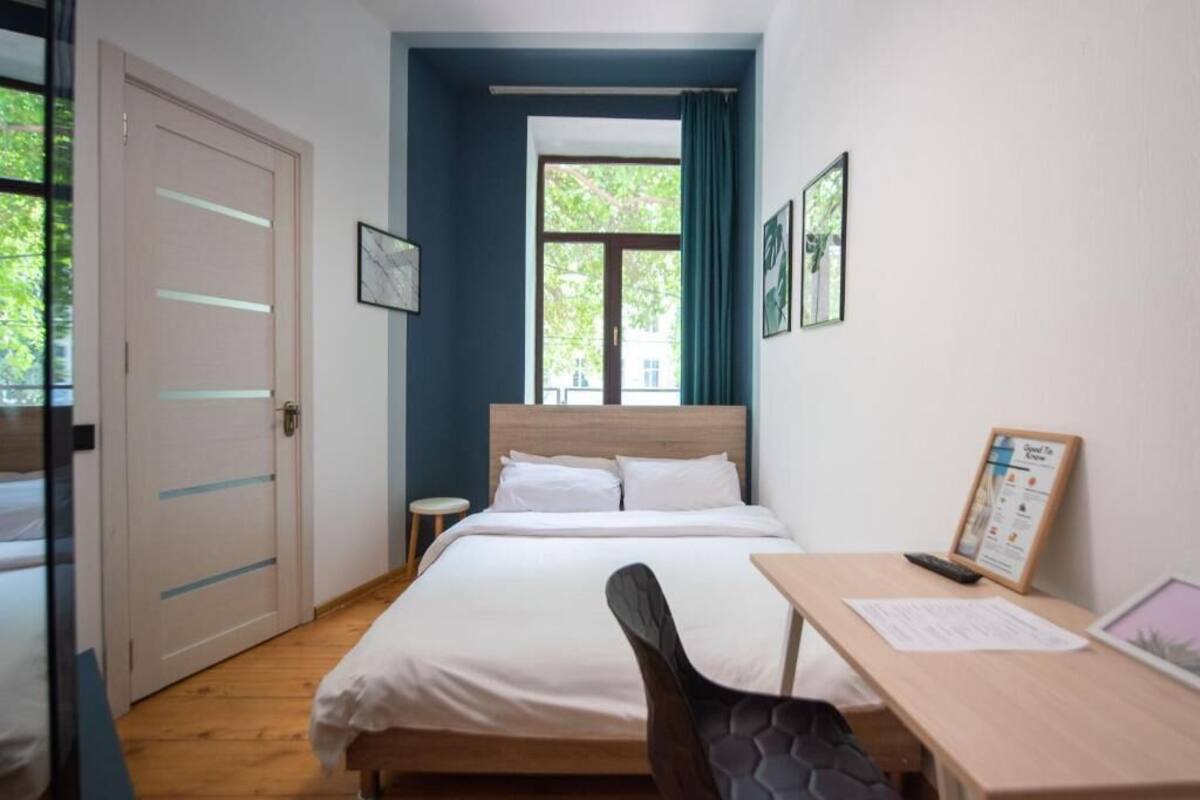 A hotel room with a bed, a desk, a chair, a window with curtains, and a door.