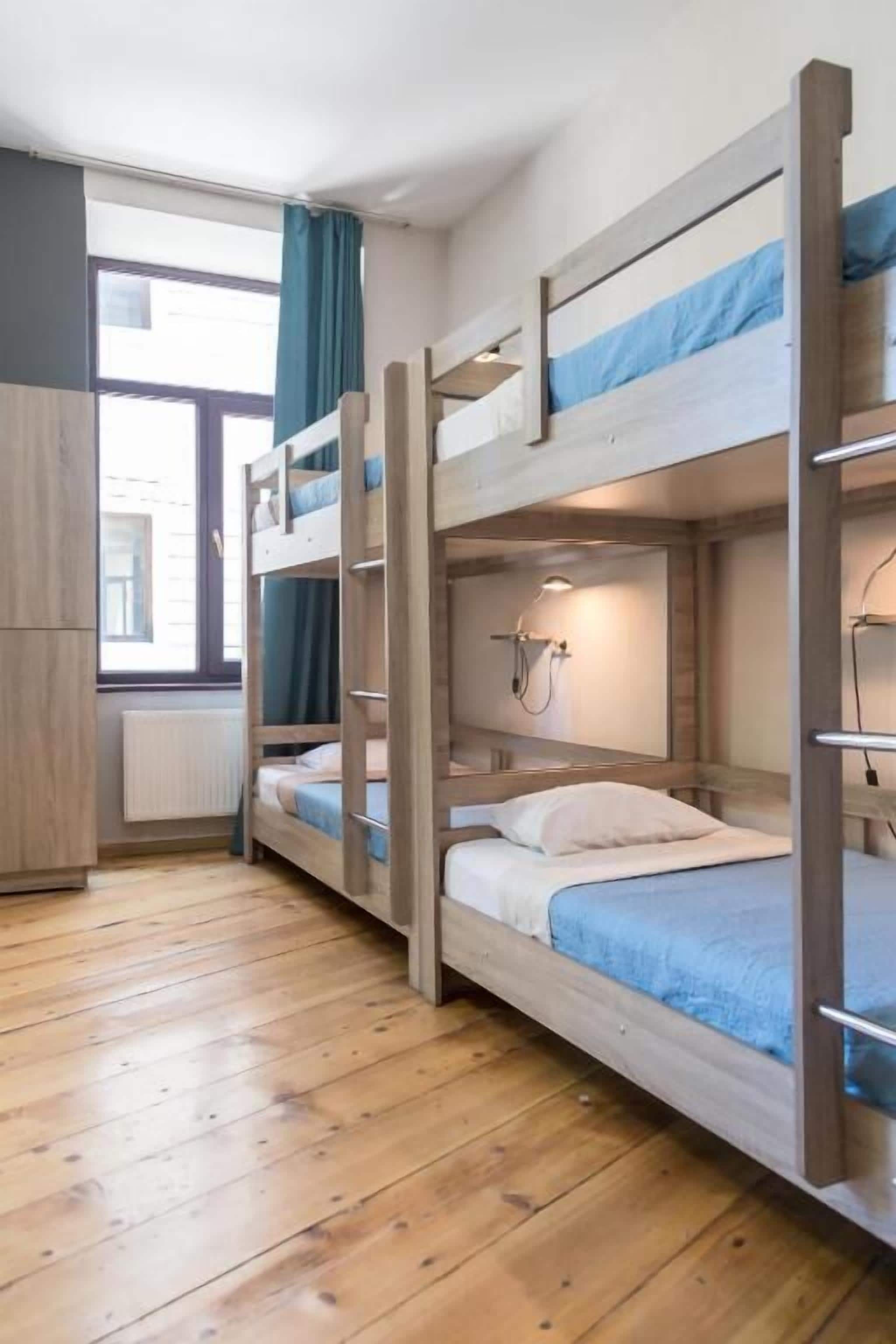A bunk bed room with a wooden floor, a window with curtains, and a bedside lamp.