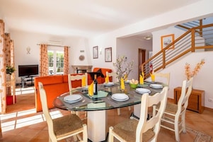Un comedor con una mesa de vidrio, sillas blancas y un sofá al fondo.