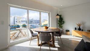 Ein modernes Wohnzimmer mit einem runden Holztisch, grauen Stühlen, einer Couch und einer großen Schiebetür zum Balkon.