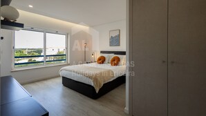 Ein modernes Schlafzimmer mit einem großen Bett, einem Schreibtisch und Blick auf eine Brücke und Grünflächen.