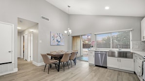 Una cocina moderna con armarios blancos, un lavamanos de acero inoxidable y una zona de comedor con mesa y sillas.