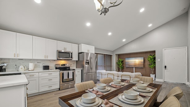 Una cocina moderna con armarios blancos, electrodomésticos de acero inoxidable y un comedor con una mesa de madera dispuesta para seis personas.