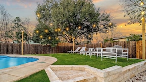 Un patio trasero con piscina, terraza de madera y zona de estar con sillas y una mesa.