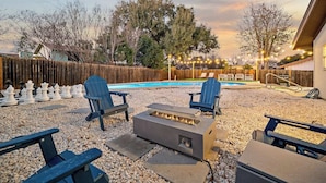 Un patio trasero con piscina, sillas Adirondack, un brasero y una valla de madera.
