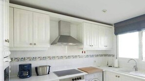 Een keuken met witte kasten, een fornuis, een spoelbak en een raam met jaloezieën.