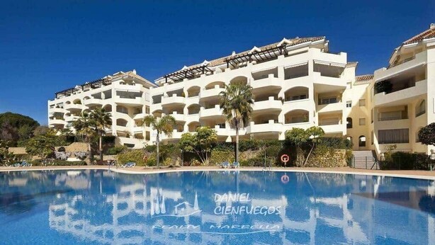 Een hotel met een groot zwembad, meerdere balkons en palmbomen.