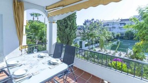 Un balcón con mesa lista para comer, con vistas a una cancha de tenis y zonas verdes.