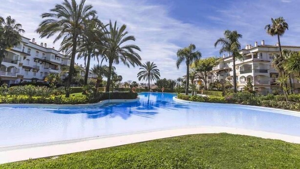 Una piscina rodeada de palmeras y edificios blancos con balcones.