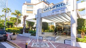 L'ingresso di un hotel con una tettoia, palme e un'auto nelle vicinanze.