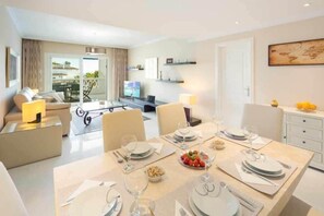 Ein modernes Wohnzimmer mit Essbereich, gedecktem Tisch, Fernseher und einem Balkon mit Sitzgelegenheit.