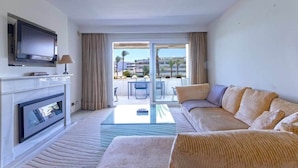 Un salon moderne doté d’un téléviseur à écran plat fixé au mur, d’un canapé, d’une table basse en verre et offrant une vue sur le balcon extérieur.