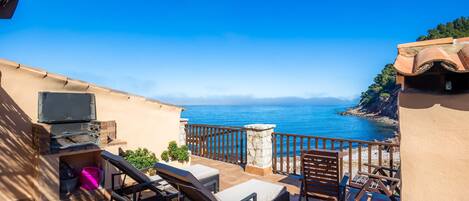 A balcony with outdoor furniture, a grill, and a view of the sea.