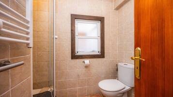 A bathroom with a shower, toilet, and a window.