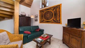 Ein gemütliches Wohnzimmer mit einem grünen Sofa, Korbsesseln, einem Holztisch und einem Fernseher auf einer Holzkommode.