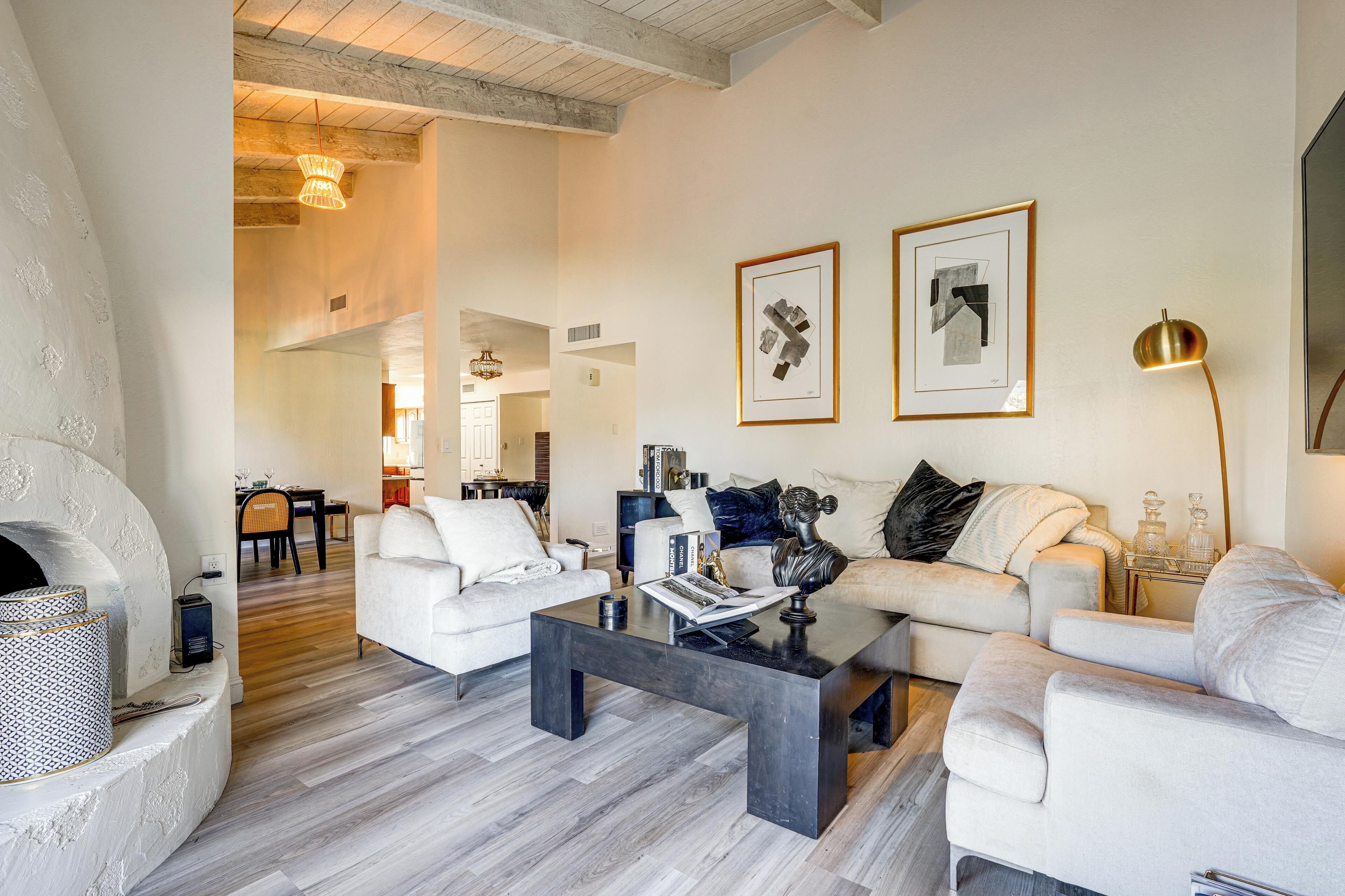 Una sala de estar moderna con chimenea, sofás blancos, una mesa de centro y obras de arte en las paredes.