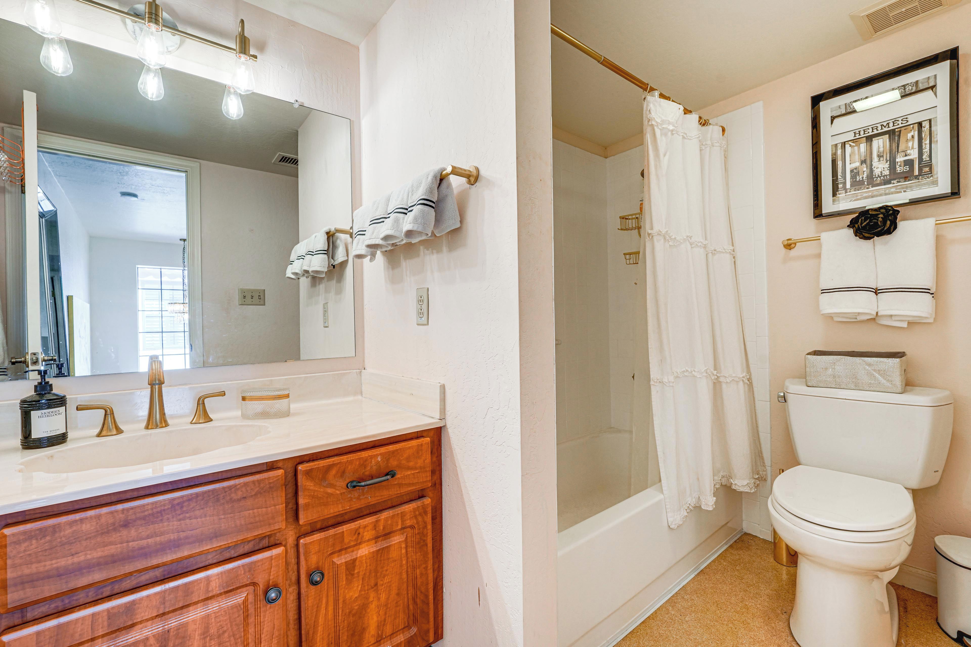 A bathroom with a white sink, wooden vanity, a large mirror, a shower with a curtain, and a toilet.