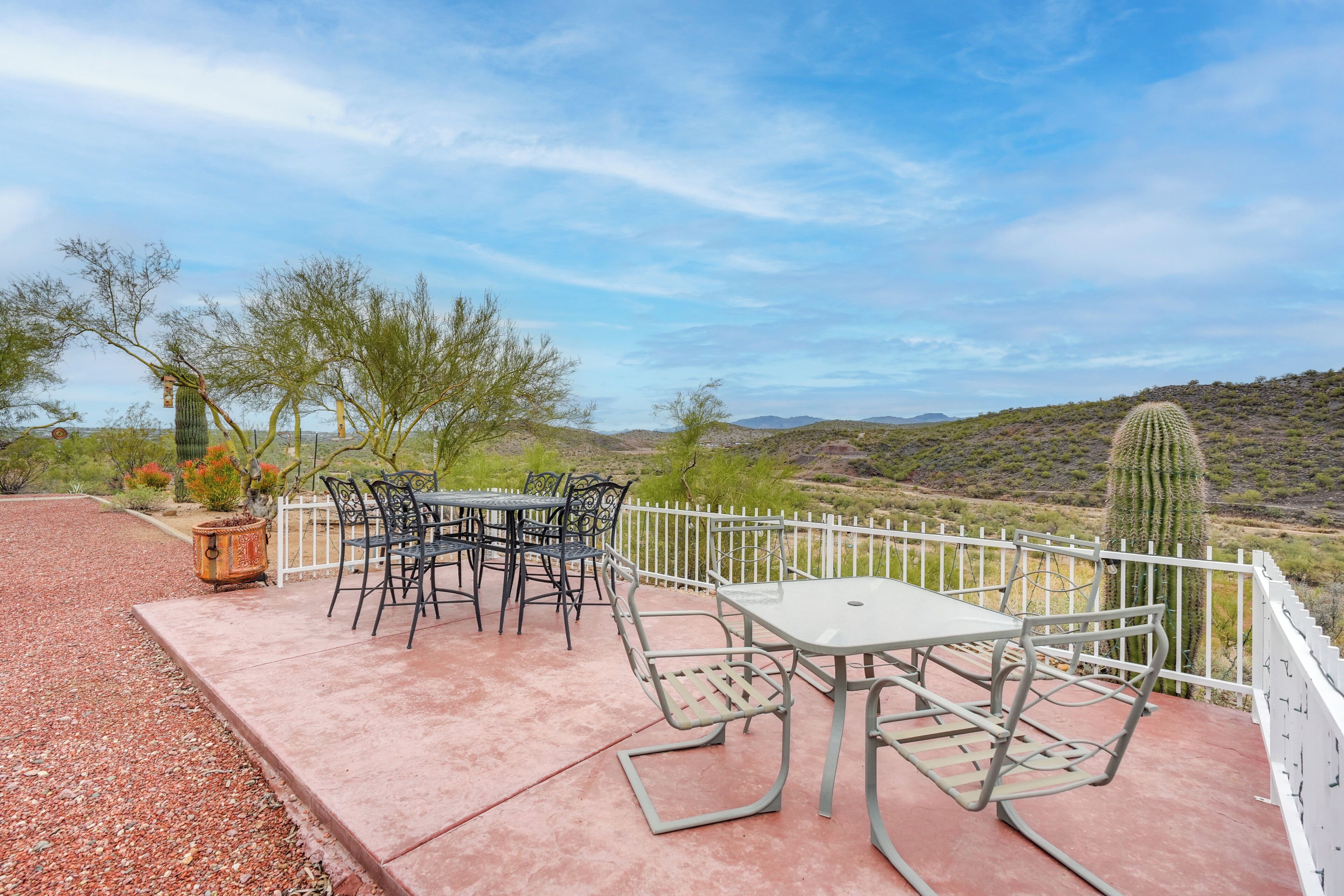 An outdoor patio with a table and chairs, surrounded by a white fence, overlooking a desert landscape with cacti and sparse vegetation.