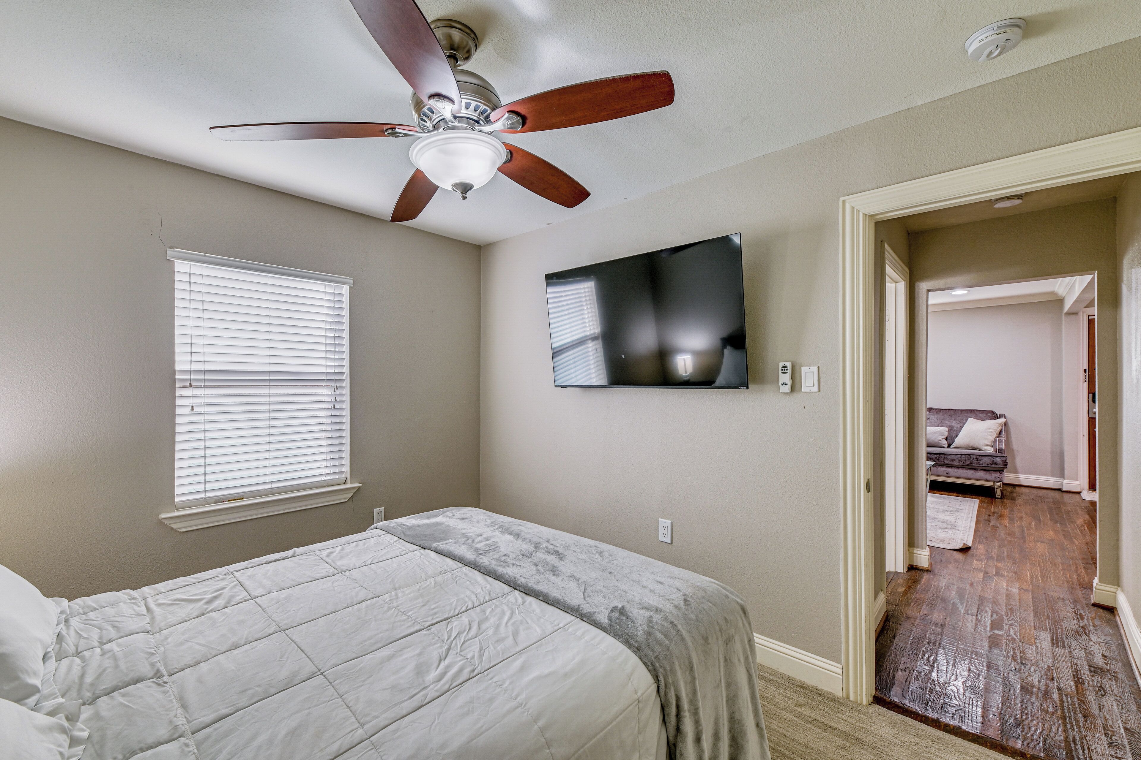 Une chambre à coucher avec un lit, un ventilateur de plafond, une télévision et une fenêtre avec des stores.