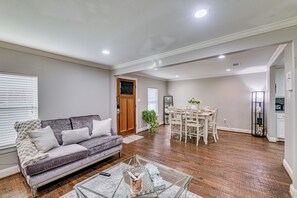 A spacious living room with a grey sofa, a glass coffee table, and a dining area with a white table and chairs. - Family-friendly Gem 1 Mi to Historic Dtwn Mckinney (McKinney)
