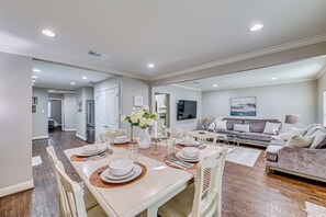 A spacious living area with a dining table set for four, a sofa, and a TV in the background. - Family-friendly Gem 1 Mi to Historic Dtwn Mckinney (McKinney)