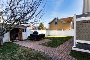 A backyard with a brick patio, a covered grill, and a white fence. - Walk to Broadway Beach! Cape May Getaway w/ Grill (Cape May)