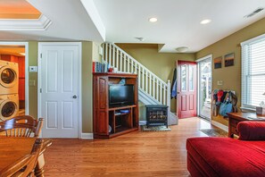 Un salón amplio con suelos de madera, un sofá rojo, un mueble de madera para el equipo de sonido y una escalera que sube a otro nivel.