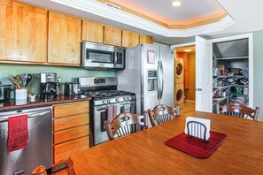 Una cocina con armarios de madera, electrodomésticos de acero inoxidable, una mesa de comedor con sillas y un mantel individual rojo.
