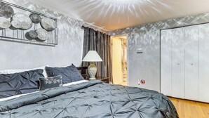 A bedroom with a large bed, a bedside table with a lamp, a wardrobe, and a wall-mounted decoration.