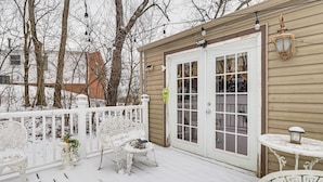 A snow-covered deck with white outdoor furniture, a white door, and a small table with a lantern.