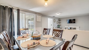 Uma sala de jantar com mesa de vidro, cadeiras e cozinha ao fundo.