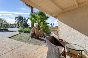 Un patio con una silla y una mesa de mimbre, una palmera y una casa al fondo.