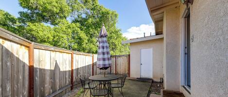 A patio with a table and chairs, a striped umbrella, and a wooden fence.