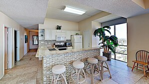 A modern kitchen with white cabinets, a central island with stools, a refrigerator, and a microwave. - Shorefront Corner PH, 3br: Suntide III - Unit 1201 (South Padre Island)