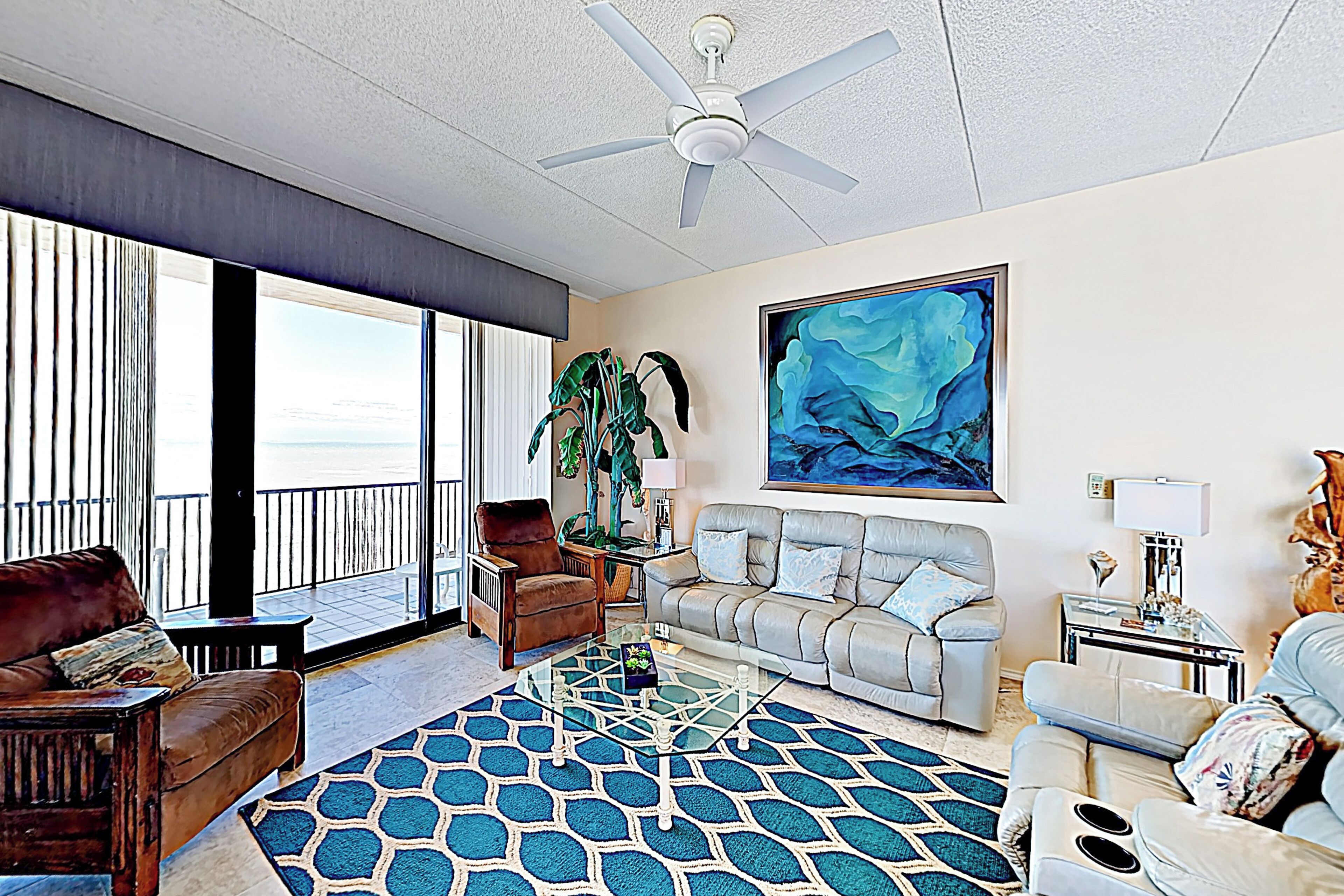 A spacious living room with a large window, a ceiling fan, a sofa, a coffee table, and a painting on the wall.