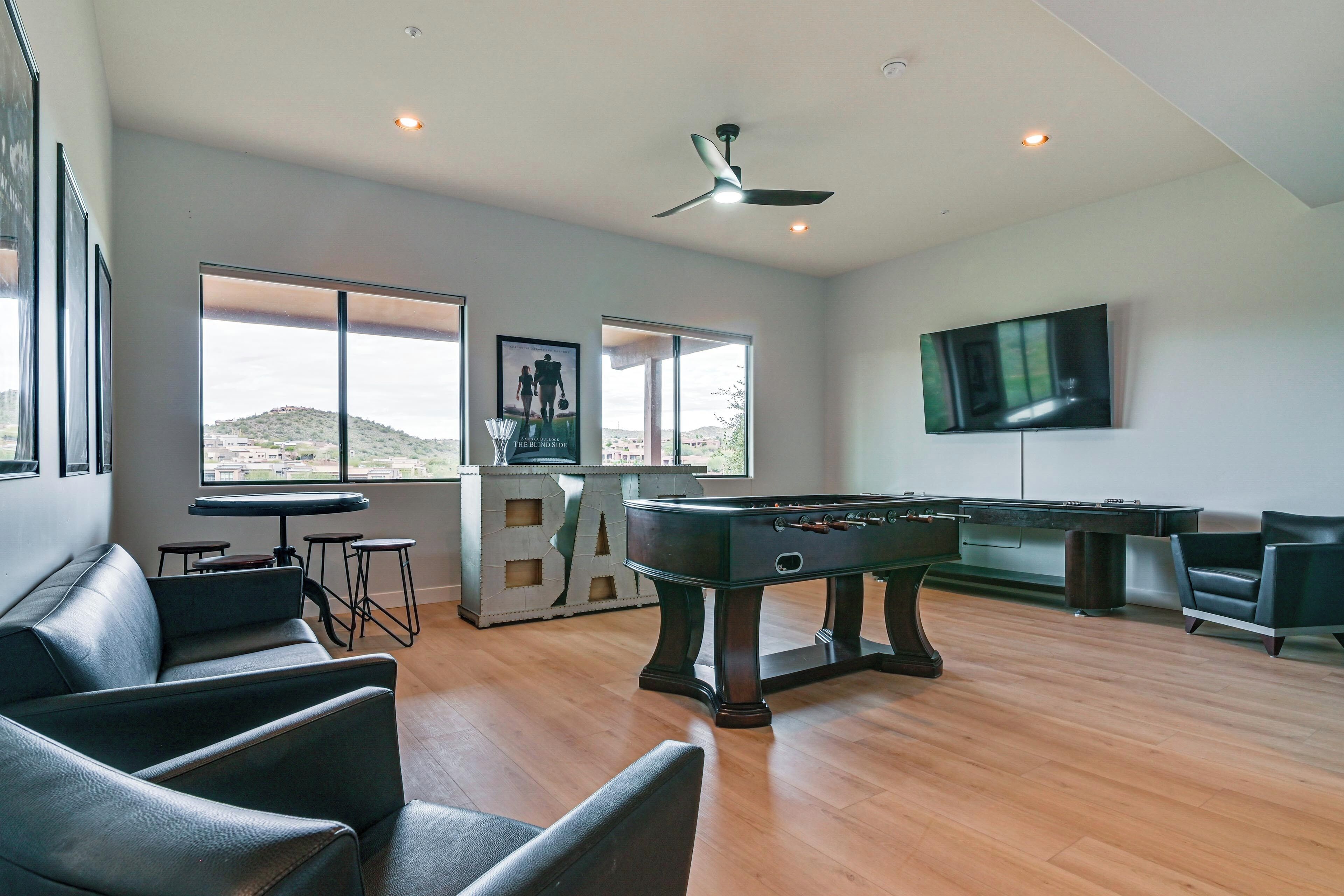 A modern living room with a pool table, comfortable seating, a television, and large windows offering a view of the hills.