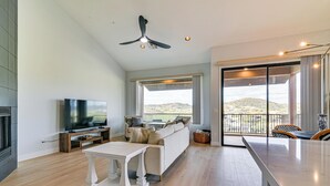 Een ruime woonkamer met een flatscreen televisie, een witte bank en een eethoek met een groot raam met uitzicht op de heuvels.