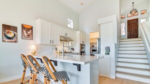 Een moderne keuken met witte kasten, een centraal eiland en een eethoek met rieten stoelen.