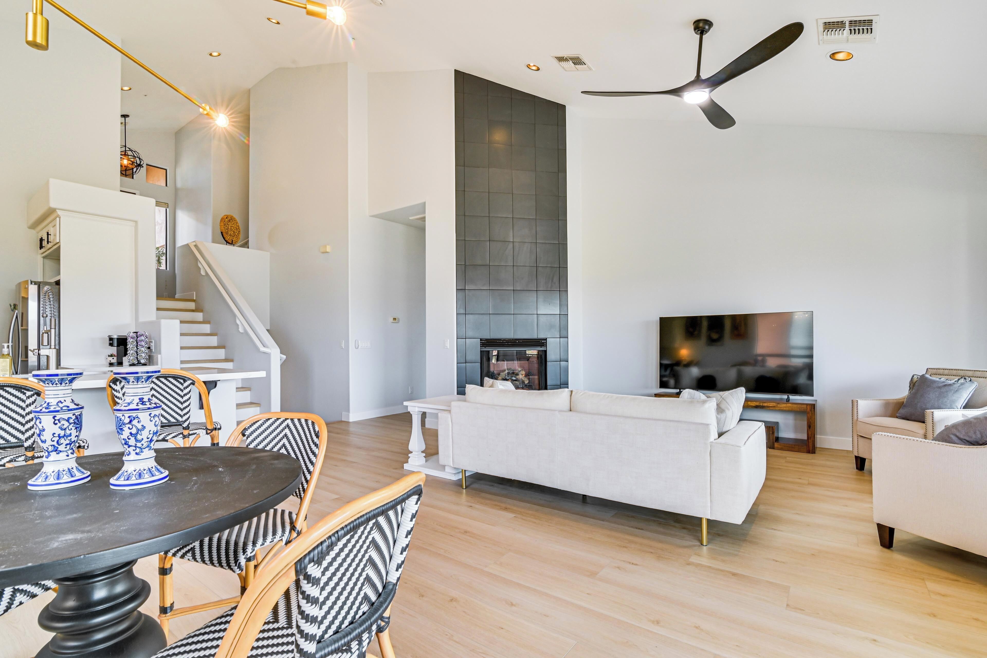 A modern living room with a fireplace, white sofas, and a dining area with patterned chairs.