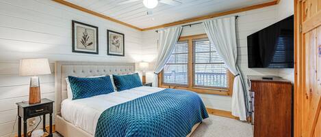 Un dormitorio con cama, mesita de noche, televisor y ventana con cortinas.
