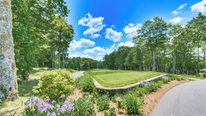 Ein Golfplatz mit Steinmauer, gepflegtem Rasen und violetten Blumen.