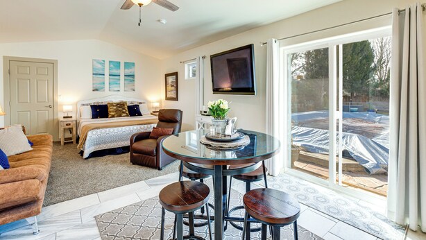 A spacious living area with a glass-top dining table, a ceiling fan, a large window with curtains, and a view of the backyard. - 4 Mi to Dtwn! Grand Junction Stay w/ Private Pool (Grand Junction)